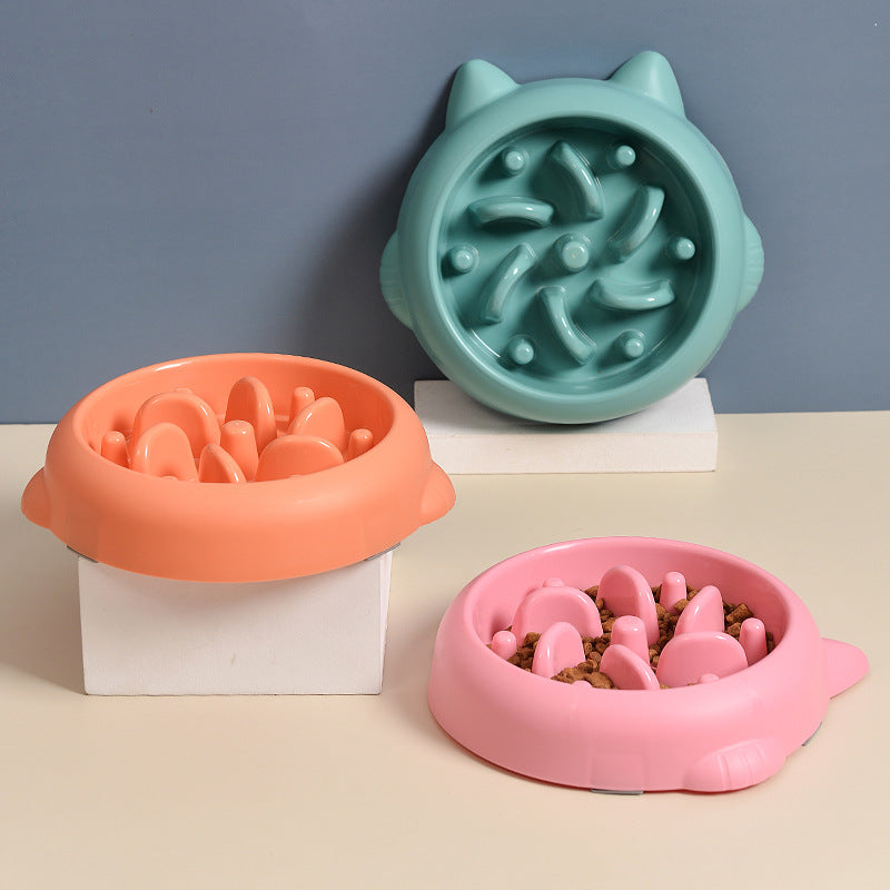 Orange and pink slow feeder bowls filled with kibble next to a teal maze bowl
